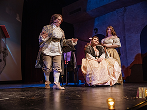 Three Actresses in period costumes on theatre stage during opera performance.