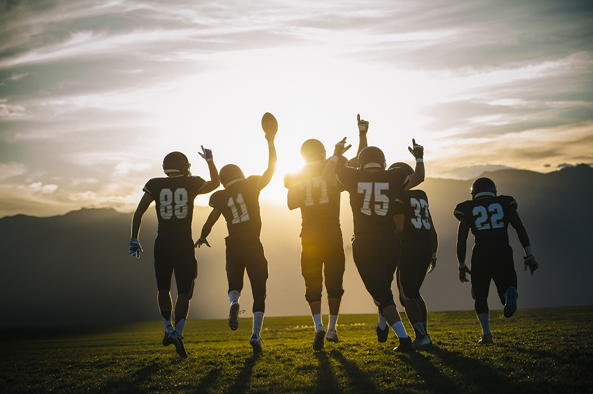 Rear view of college football team celebrating at sunset