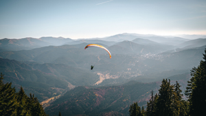 A scenic landscape of a paraglider flying in the mountains